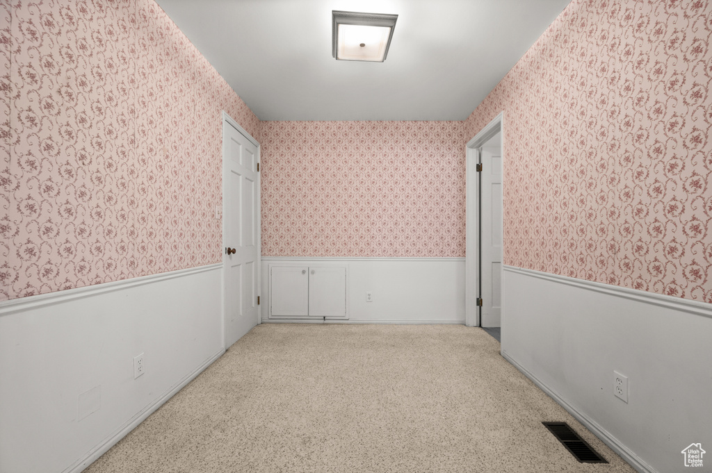 Carpeted empty room featuring wallpapered walls and a wainscoted wall