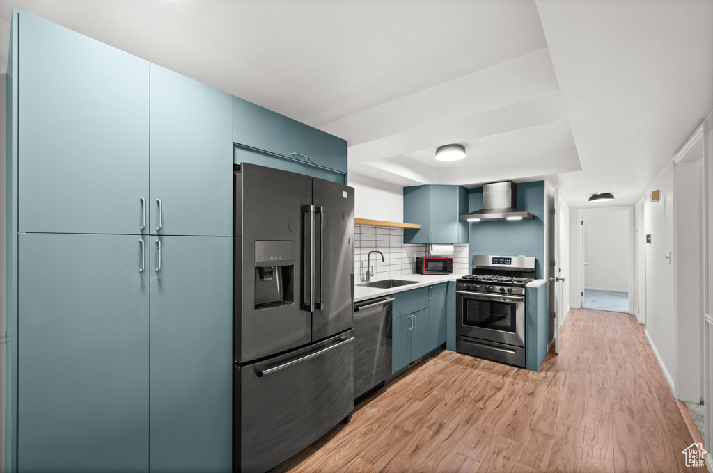 Kitchen featuring stainless steel appliances, wall chimney range hood, a sink, open shelves, and light wood-style flooring