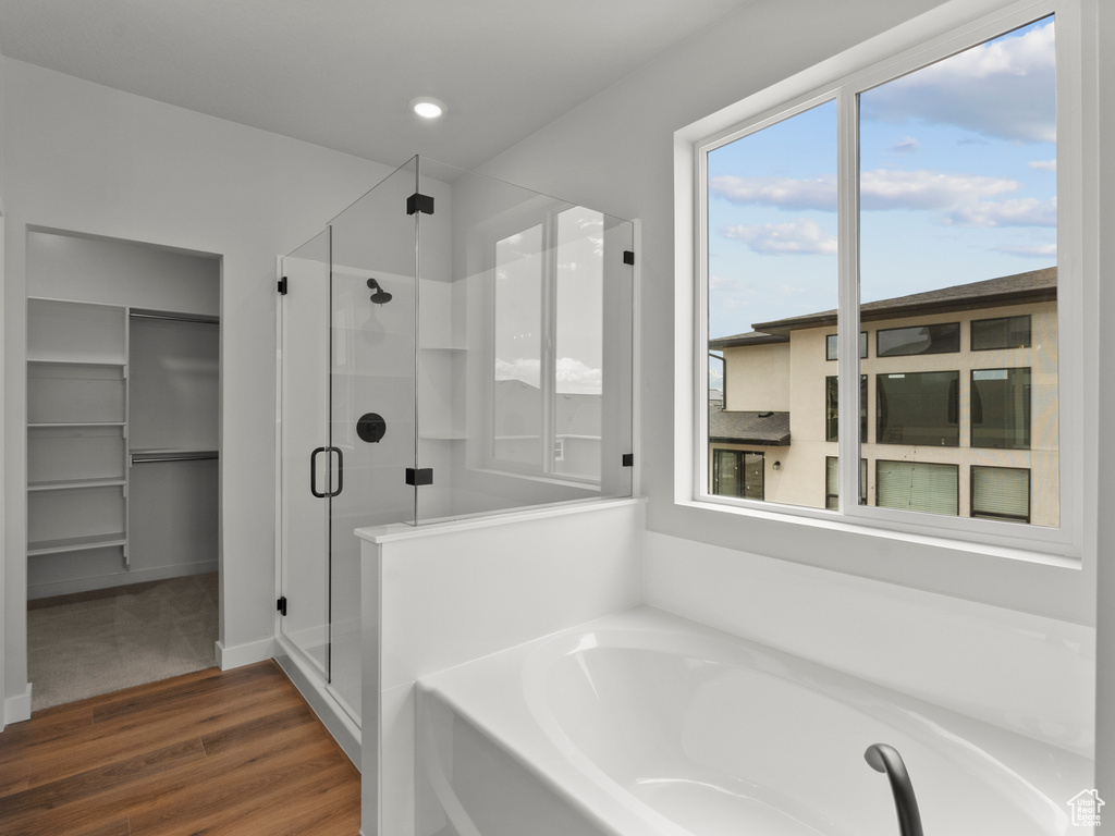 Bathroom featuring a stall shower, a garden tub, wood finished floors, plenty of natural light, and recessed lighting