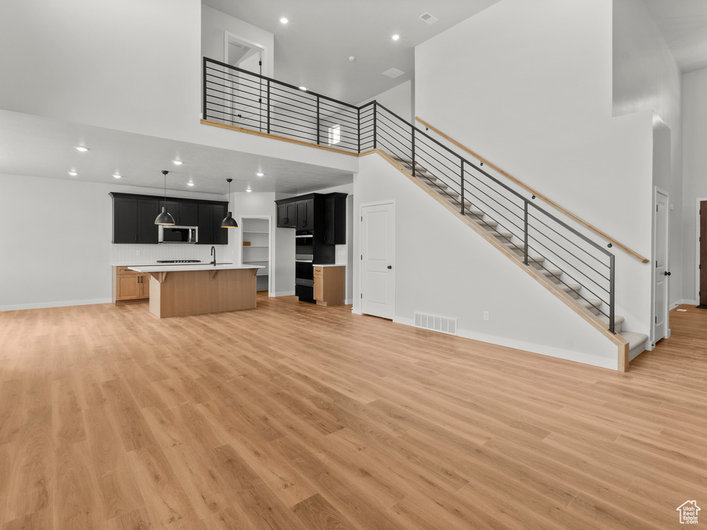 Unfurnished living room with a high ceiling, light wood-type flooring, stairs, and recessed lighting