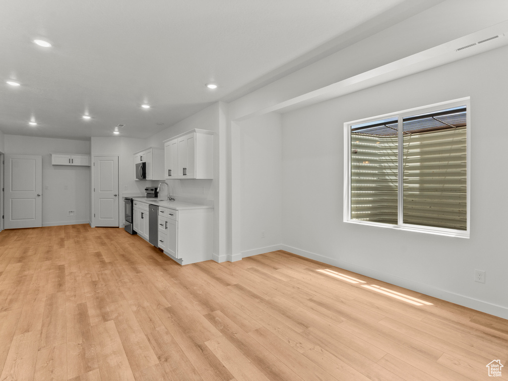 Kitchen with stainless steel appliances, light wood-style floors, white cabinetry, light countertops, and recessed lighting