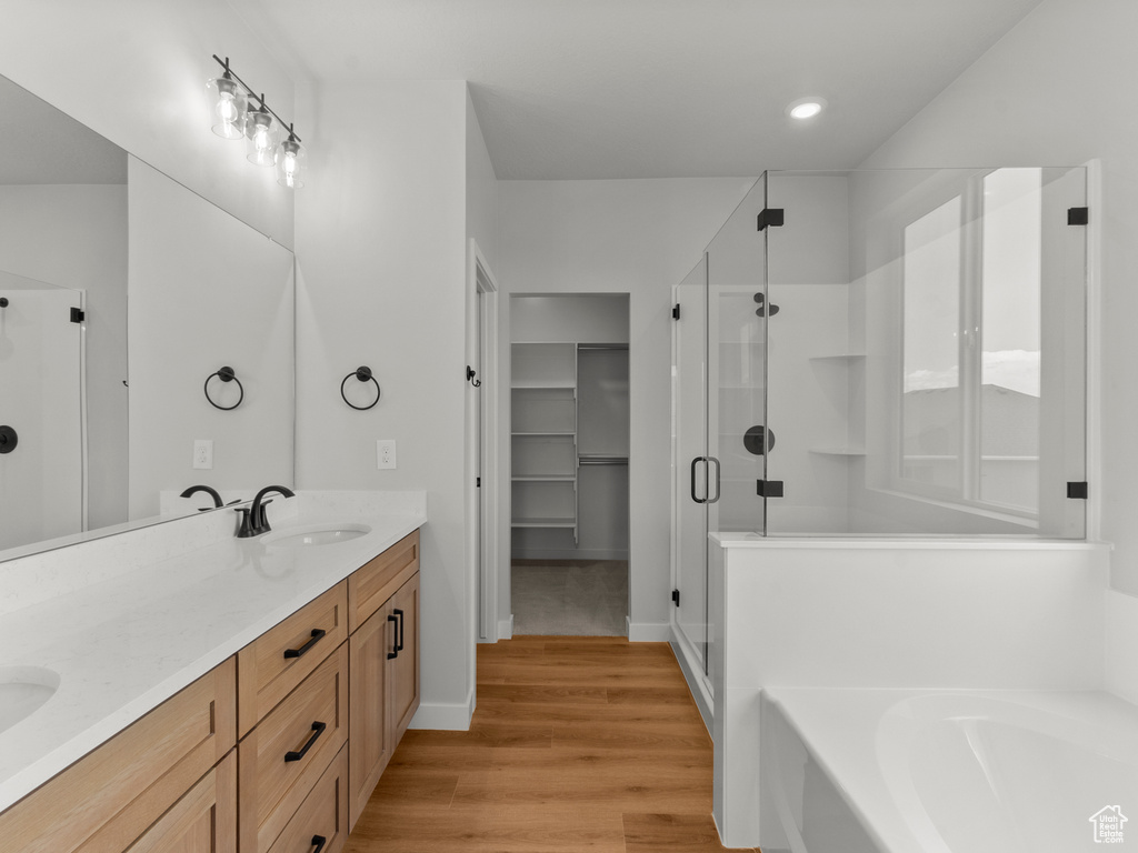 Full bathroom featuring a shower stall, a garden tub, double vanity, wood finished floors, and recessed lighting