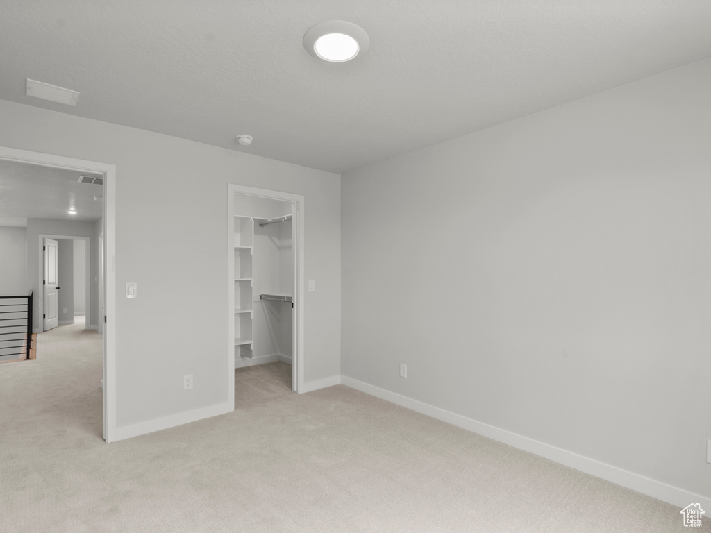 Unfurnished bedroom with light colored carpet, a walk in closet, and a closet