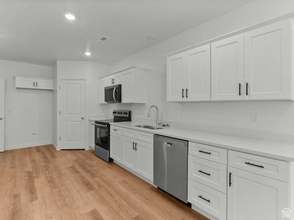 Kitchen with stainless steel appliances, white cabinetry, recessed lighting, light wood-type flooring, and light countertops