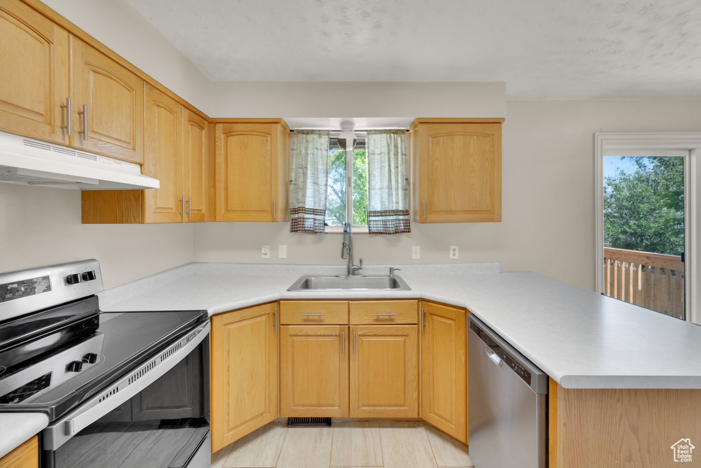 Kitchen with stainless steel appliances, under cabinet range hood, a sink, a peninsula, and light countertops