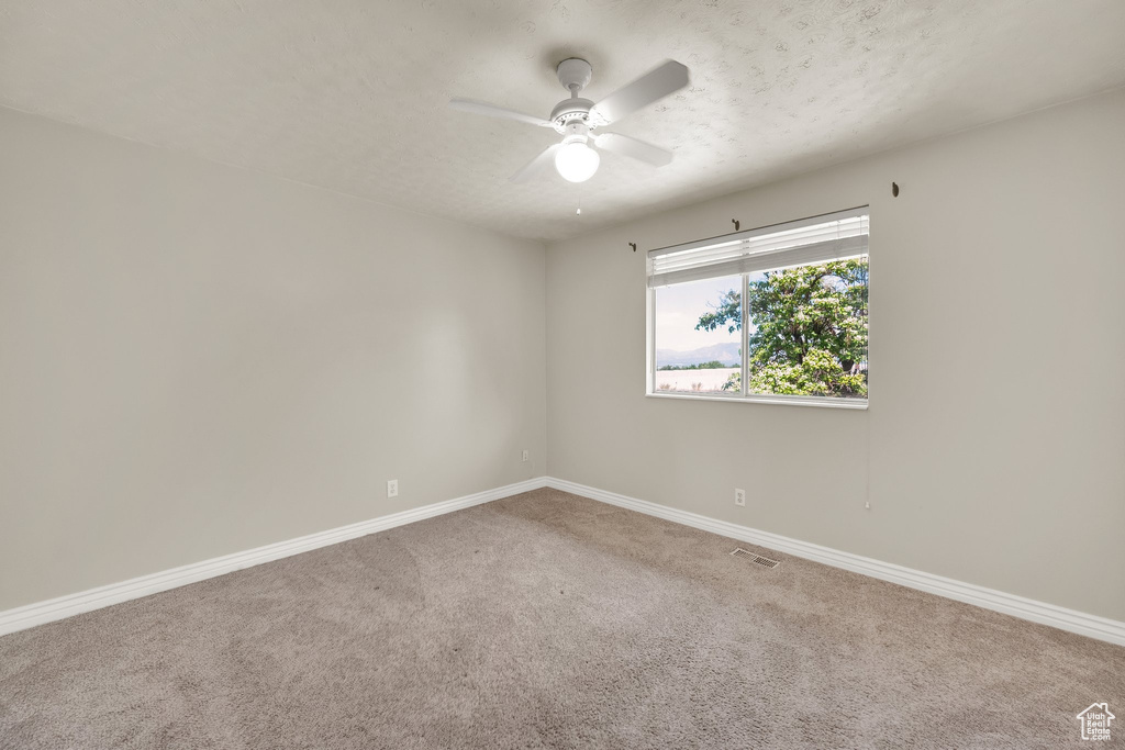 Carpeted spare room featuring baseboards, ceiling fan, and a textured ceiling