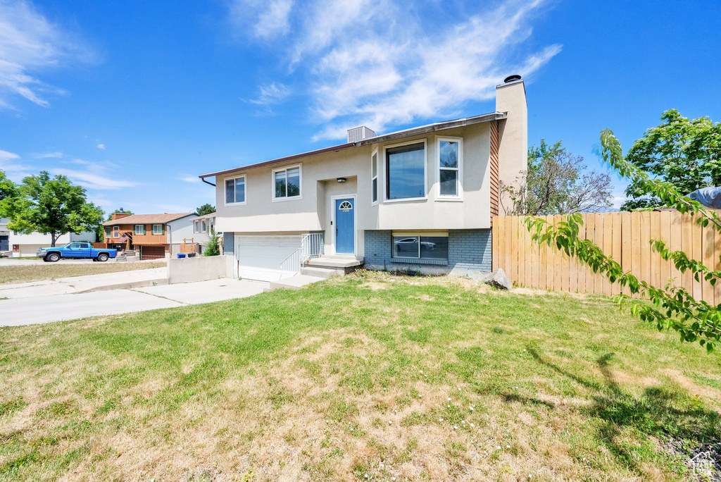 Split foyer home featuring a garage, concrete driveway, a chimney, stucco siding, and brick siding