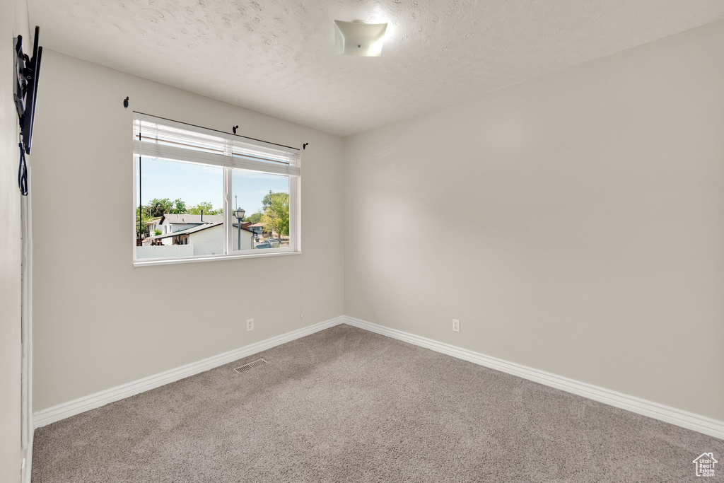 Empty room with carpet floors, baseboards, and a textured ceiling