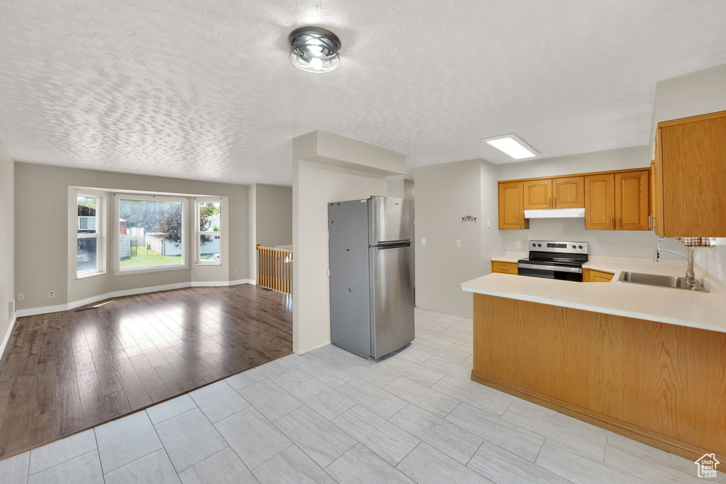 Kitchen featuring stainless steel appliances, a sink, open floor plan, under cabinet range hood, and light countertops