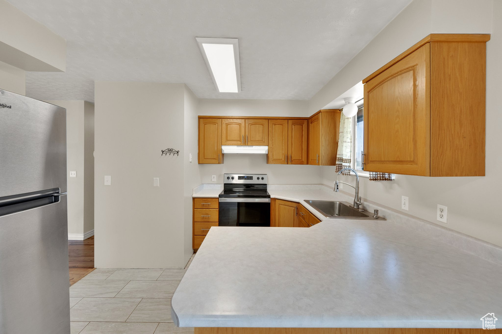 Kitchen with appliances with stainless steel finishes, a sink, light countertops, under cabinet range hood, and a peninsula
