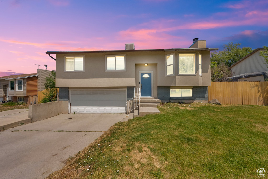 Raised ranch featuring a garage, stucco siding, concrete driveway, and a chimney