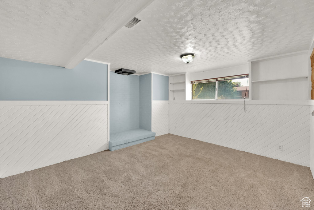 Carpeted empty room with wainscoting, wood walls, and a textured ceiling