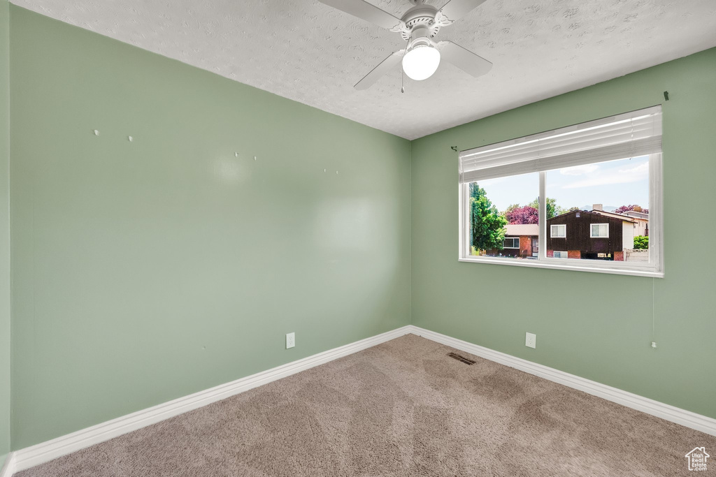 Carpeted empty room with baseboards, a textured ceiling, and a ceiling fan