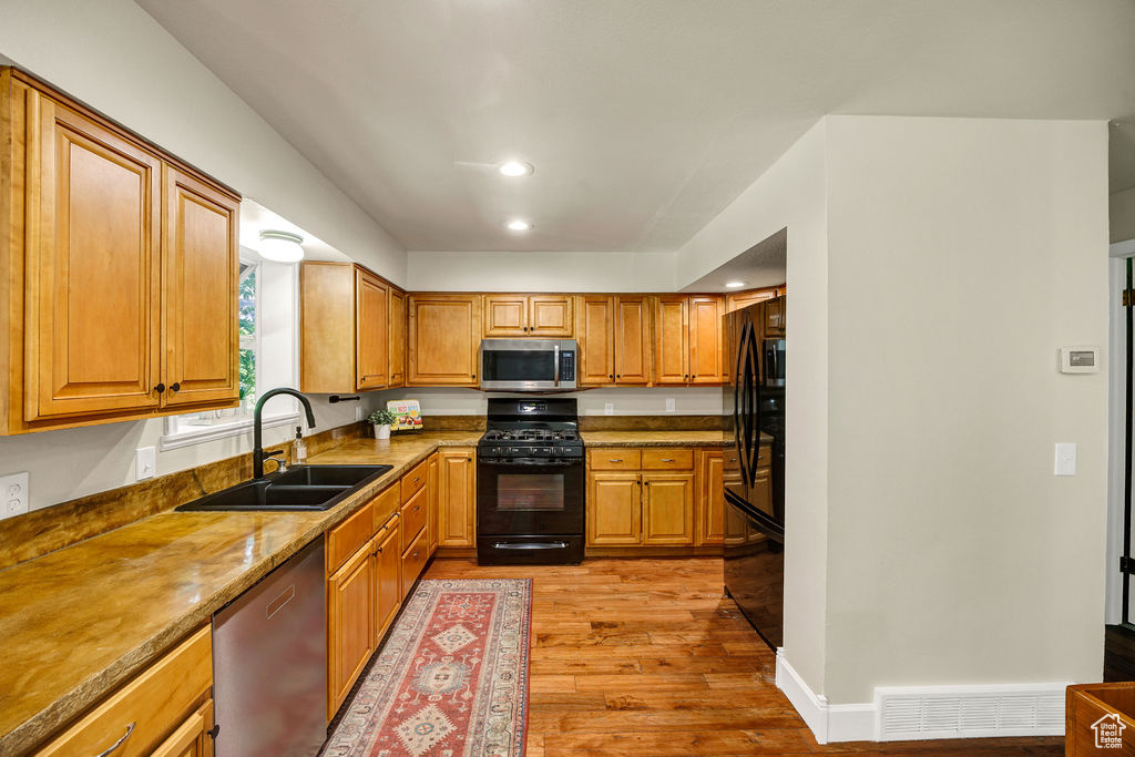 Kitchen with black appliances, a sink, light wood-type flooring, recessed lighting, and brown cabinetry
