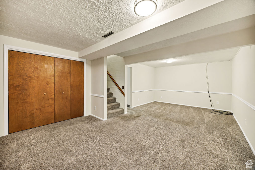 Finished basement with carpet floors, stairs, baseboards, and a textured ceiling