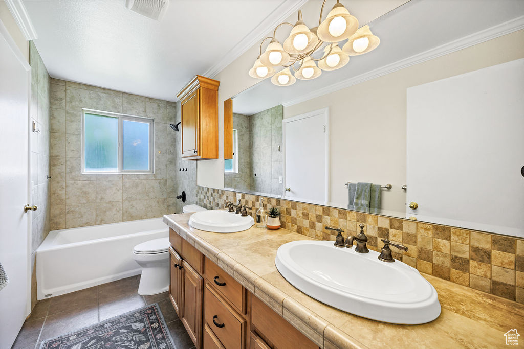Full bathroom with toilet, double vanity, decorative backsplash, tile patterned floors, and ornamental molding