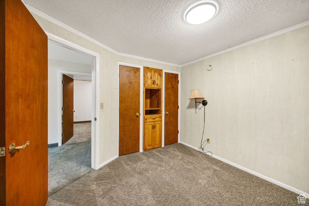 Spare room featuring dark carpet, a textured ceiling, ornamental molding, and baseboards