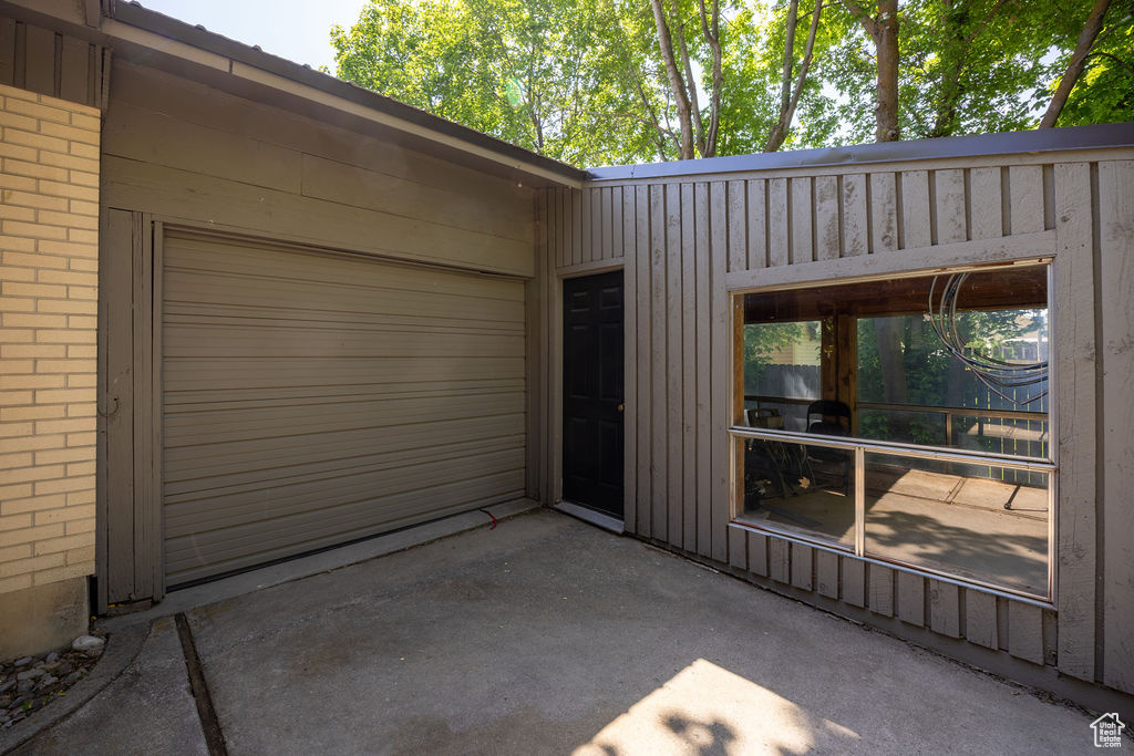View of exterior entry featuring brick siding, a patio area, driveway, and an attached garage
