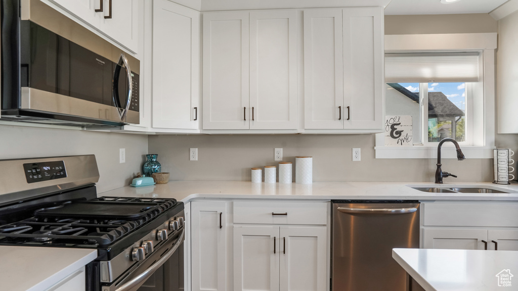 Kitchen with appliances with stainless steel finishes, a sink, and white cabinetry