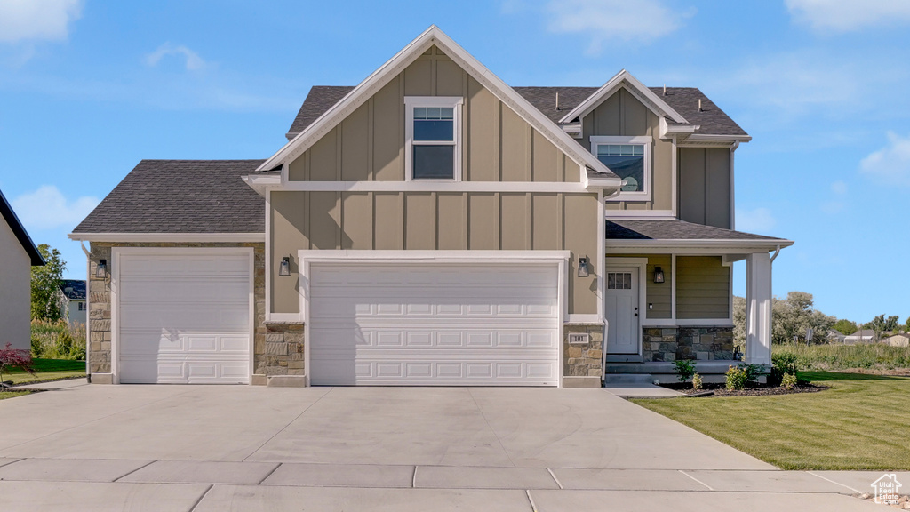 Craftsman house featuring stone siding, board and batten siding, driveway, roof with shingles, and a front yard