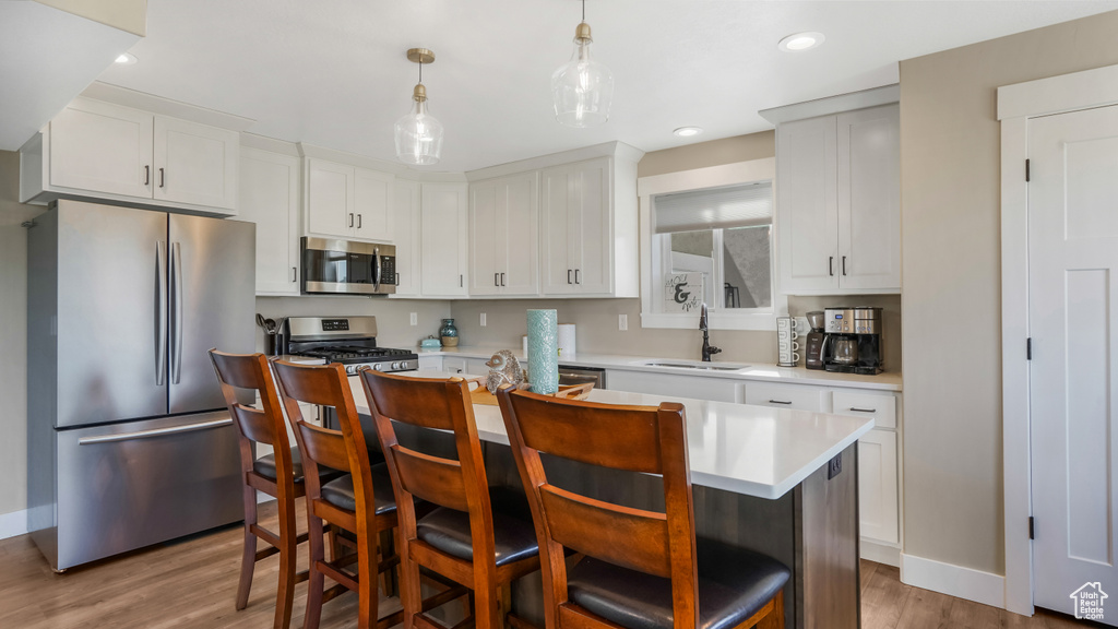 Kitchen featuring appliances with stainless steel finishes, a sink, light wood-type flooring, a kitchen island, and light countertops
