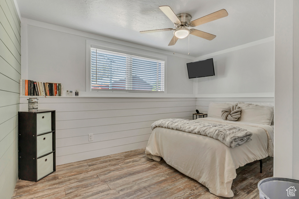 Bedroom featuring wooden walls, wood finished floors, a ceiling fan, and ornamental molding