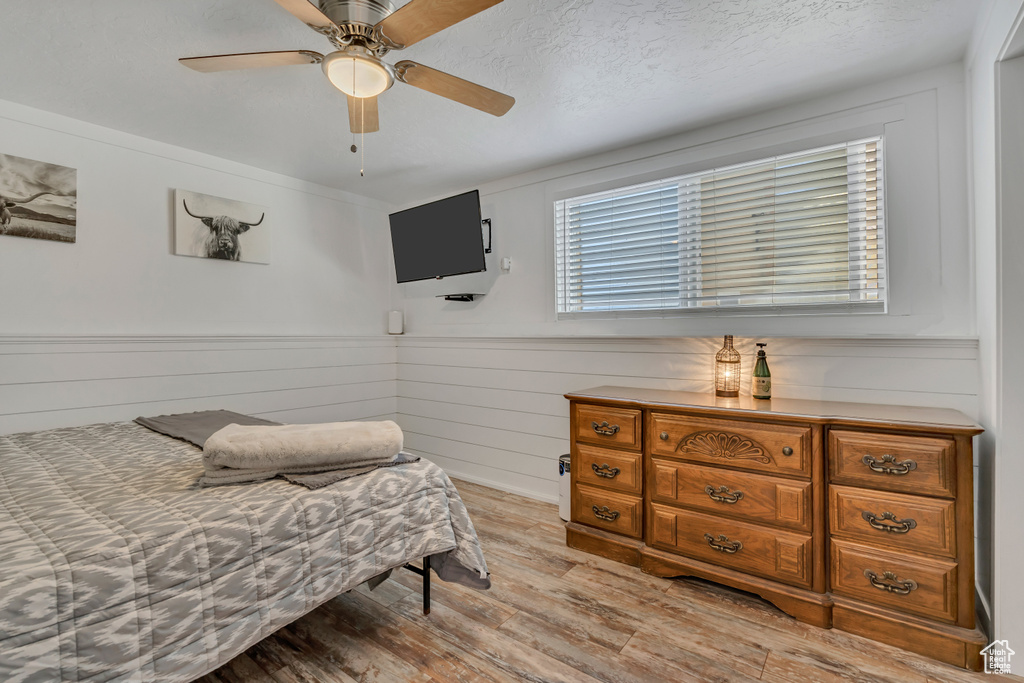 Bedroom with light wood-type flooring, wainscoting, and a ceiling fan