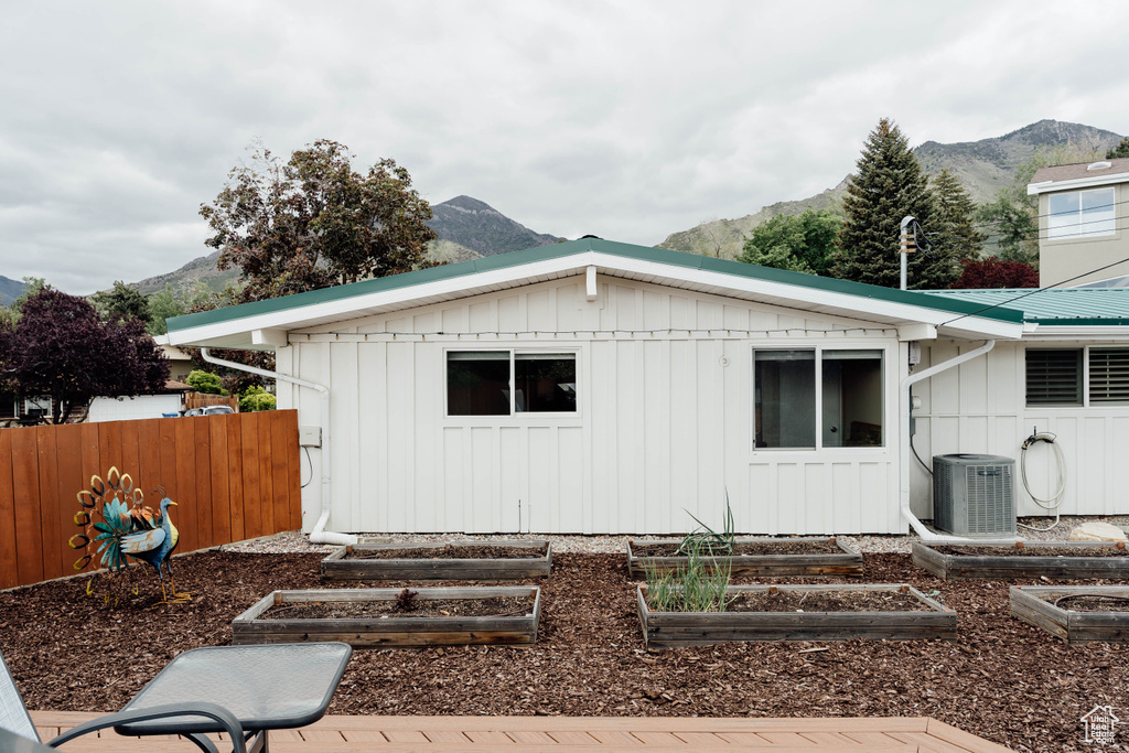 Rear view of property with board and batten siding, cooling unit, a mountain view, and a garden