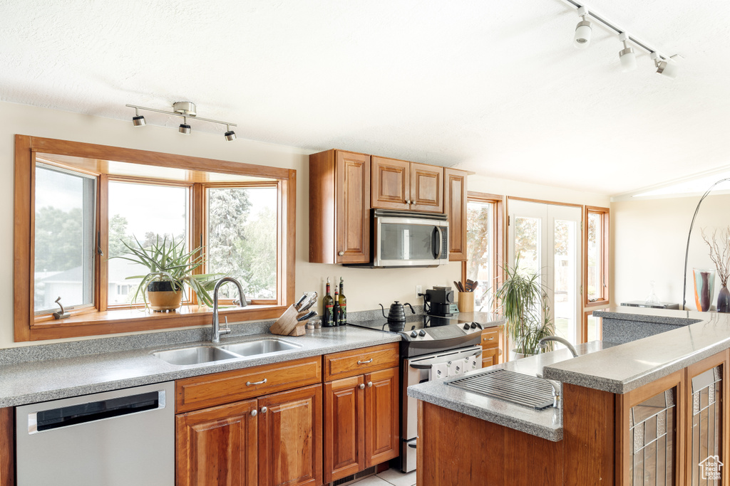 Kitchen with stainless steel appliances, a sink, rail lighting, brown cabinets, and glass insert cabinets
