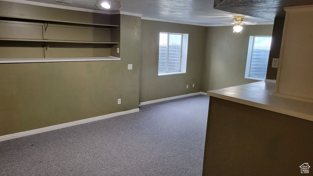 Unfurnished room featuring a ceiling fan, healthy amount of natural light, dark carpet, baseboards, and crown molding