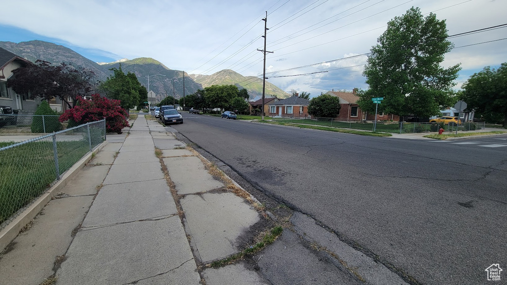 View of asphalt road featuring sidewalks, a mountain view, and curbs