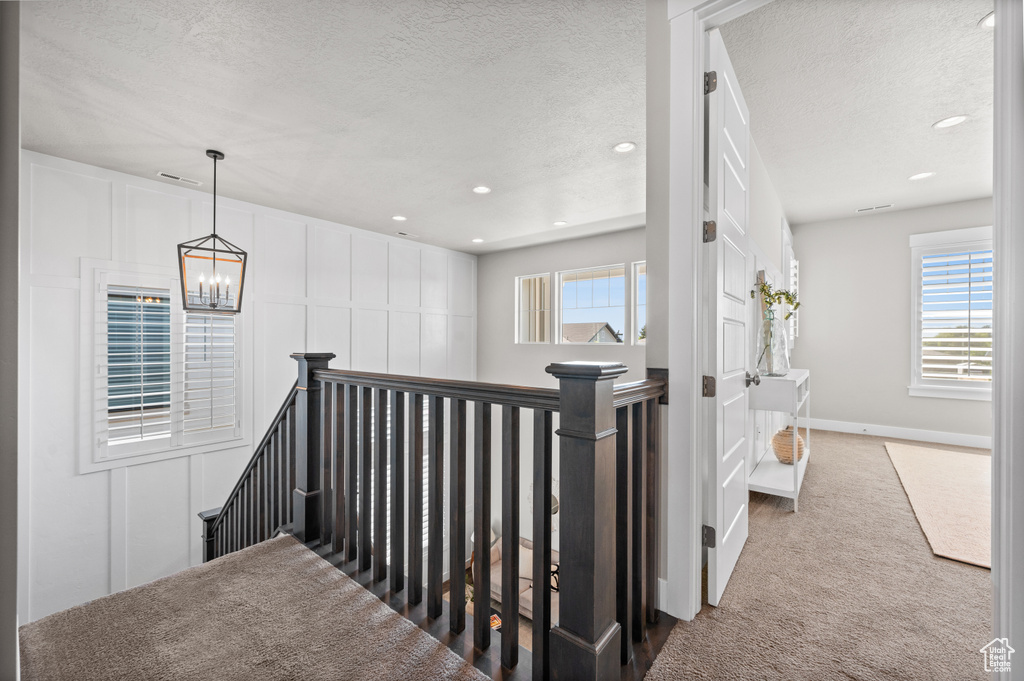 Hall with an upstairs landing, carpet floors, a textured ceiling, a chandelier, and recessed lighting