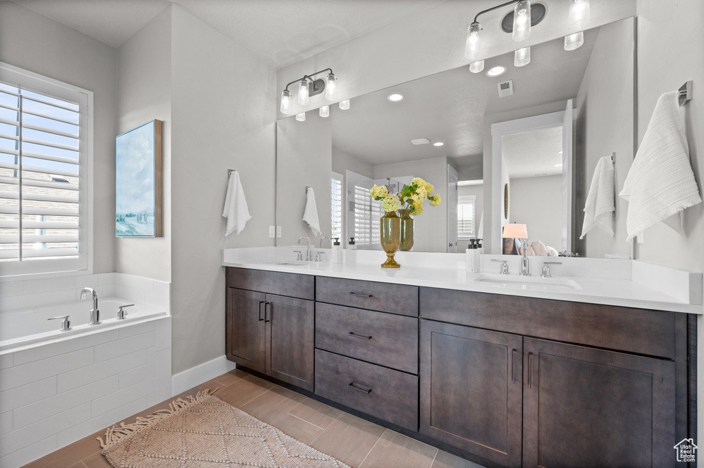 Full bath with double vanity, a bath, wood finished floors, baseboards, and connected bathroom