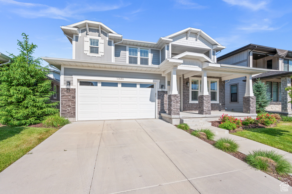 Craftsman-style home with stone siding, covered porch, concrete driveway, an attached garage, and board and batten siding