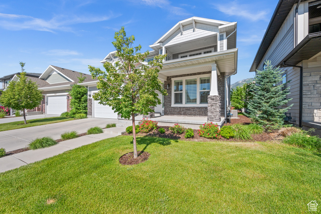 View of front of property featuring covered porch, concrete driveway, a garage, a front yard, and stone siding