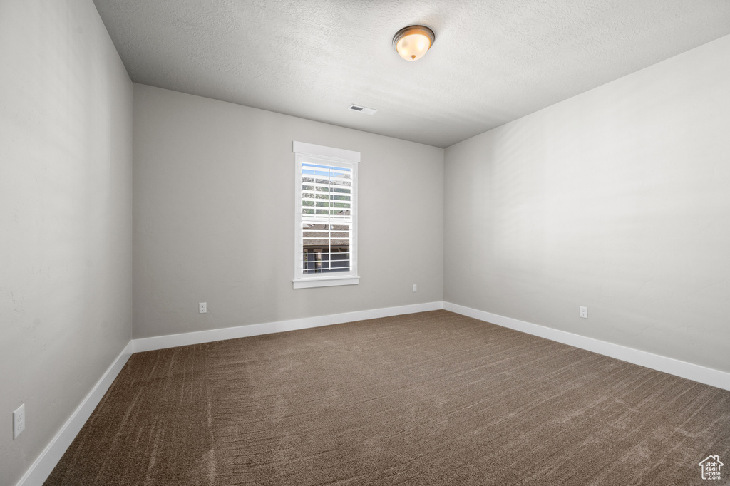 Spare room with dark colored carpet, a textured ceiling, and baseboards