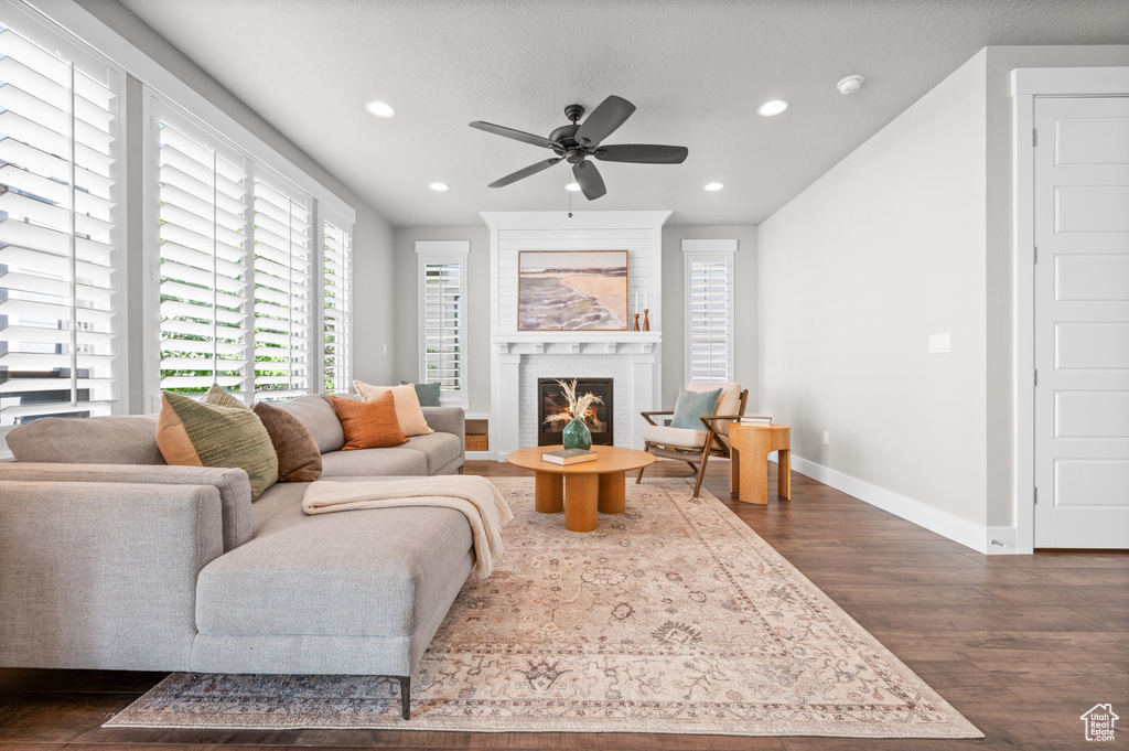 Living area with dark wood-type flooring, recessed lighting, ceiling fan, baseboards, and a fireplace