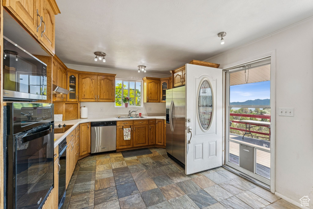Kitchen featuring appliances with stainless steel finishes, brown cabinets, light countertops, a sink, and dark stone finish flooring