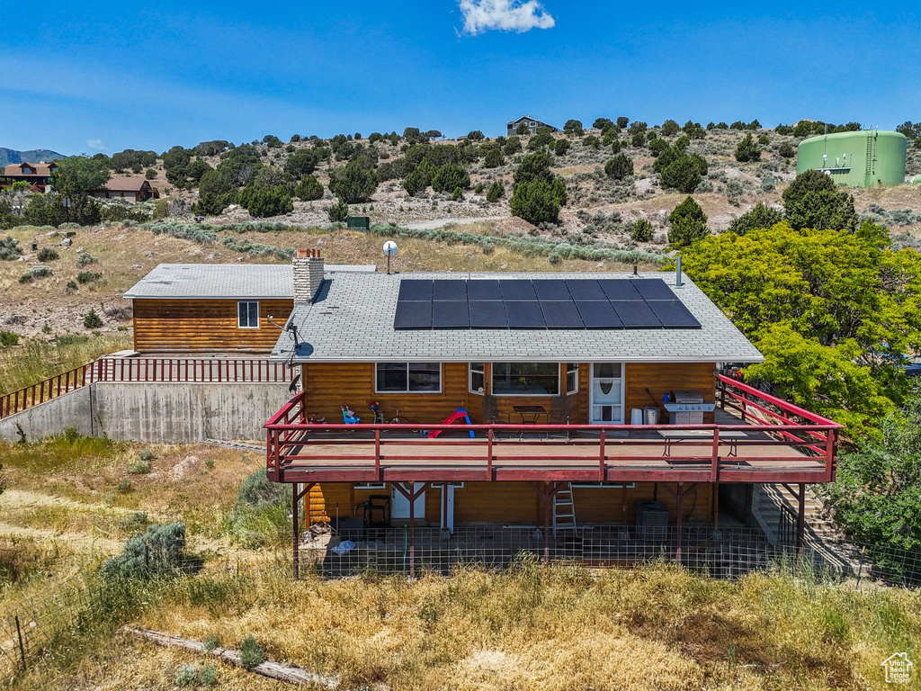 Rear view of house with a deck, roof mounted solar panels, and a chimney