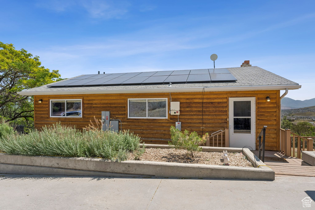 View of front of home with roof mounted solar panels, a wooden deck, and a shingled roof