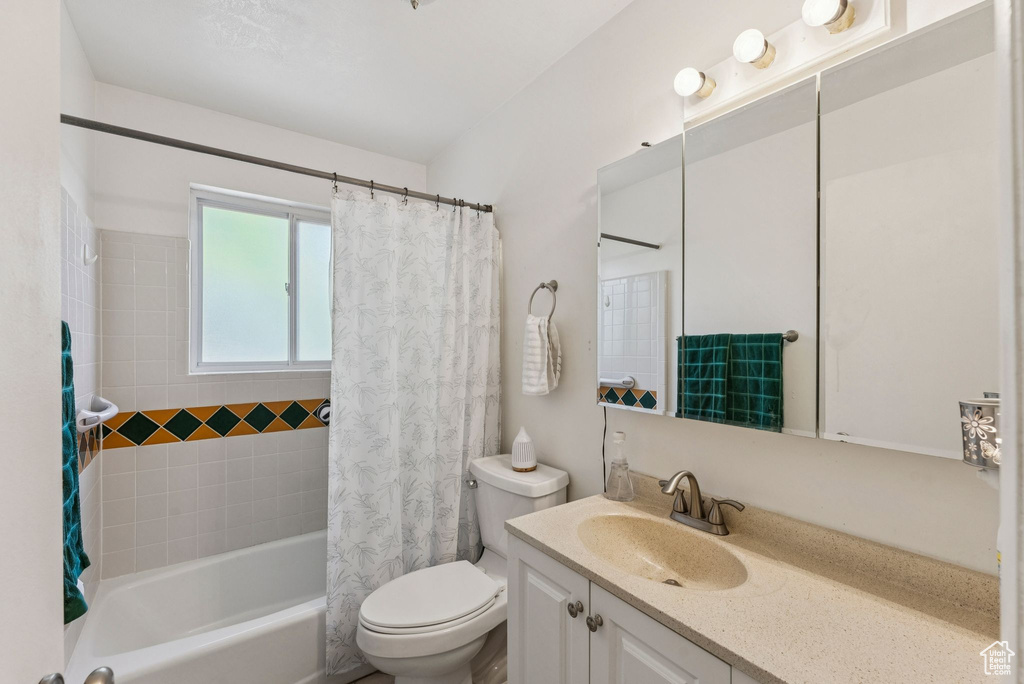 Bathroom featuring vanity, shower / bathtub combination with curtain, and toilet