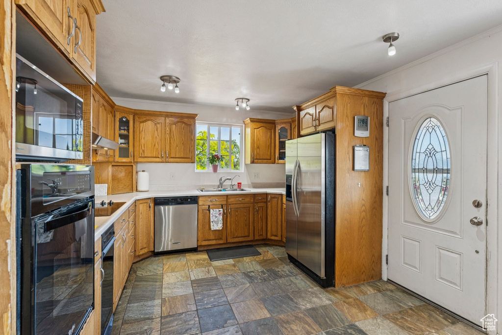 Kitchen with black appliances, brown cabinets, a sink, light countertops, and dark stone finish floors