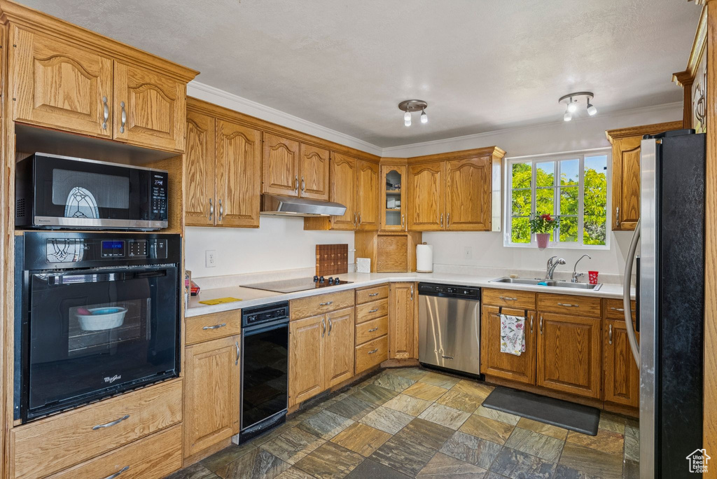 Kitchen featuring black appliances, a sink, under cabinet range hood, brown cabinetry, and stone finish floors