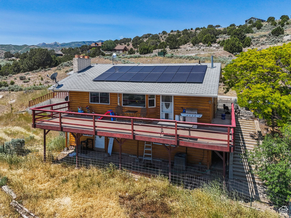 Rear view of house with a deck with mountain view, a shingled roof, and solar panels