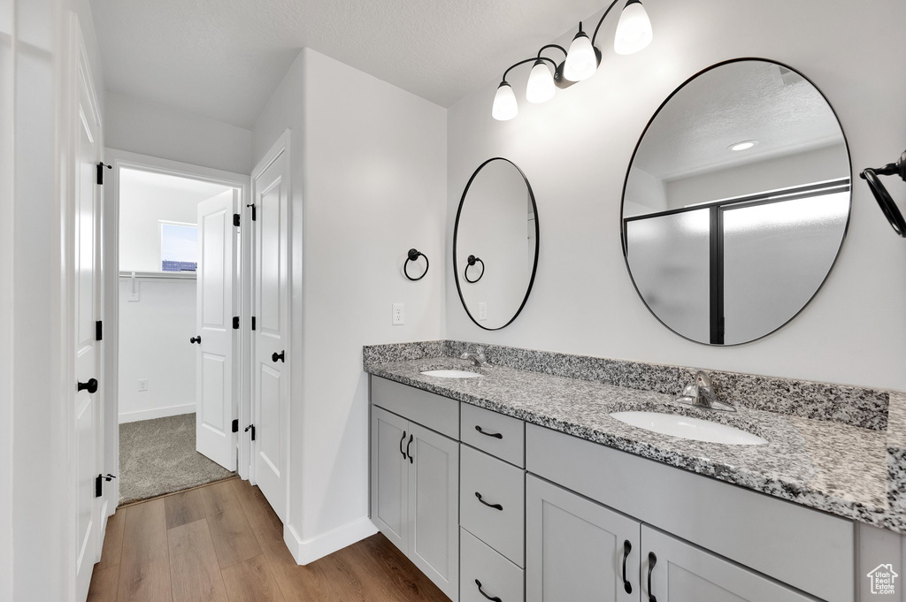 Full bath with wood finished floors, double vanity, baseboards, and a walk in closet