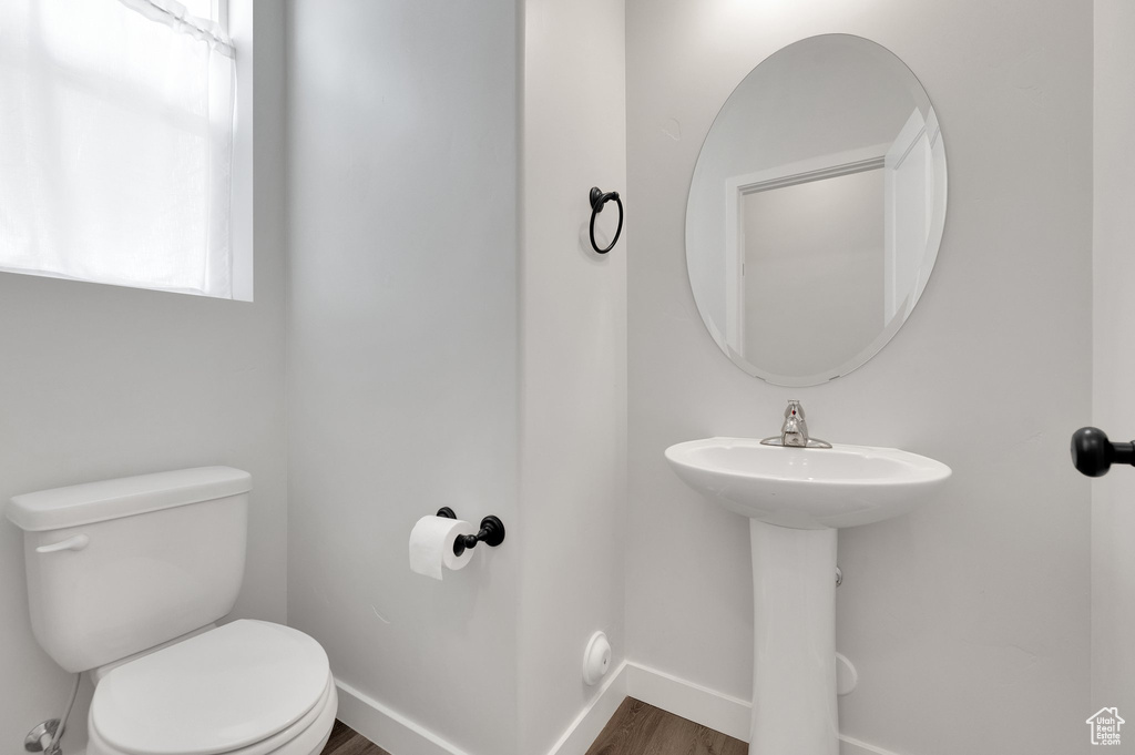 Half bathroom featuring toilet, wood finished floors, baseboards, and a sink