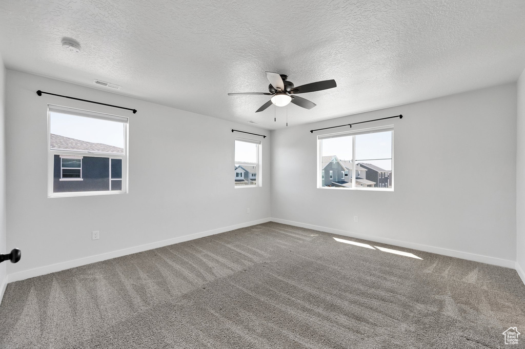 Empty room with carpet floors, ceiling fan, a textured ceiling, and baseboards