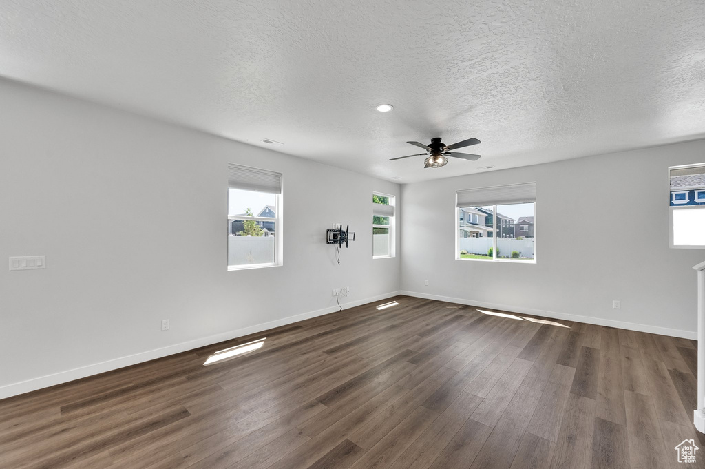 Unfurnished room featuring healthy amount of natural light, dark wood-type flooring, baseboards, ceiling fan, and a textured ceiling