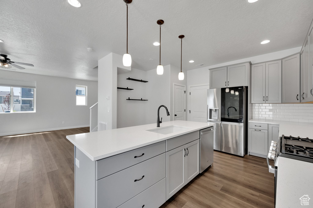 Kitchen with stainless steel appliances, a sink, gray cabinets, open floor plan, and light countertops