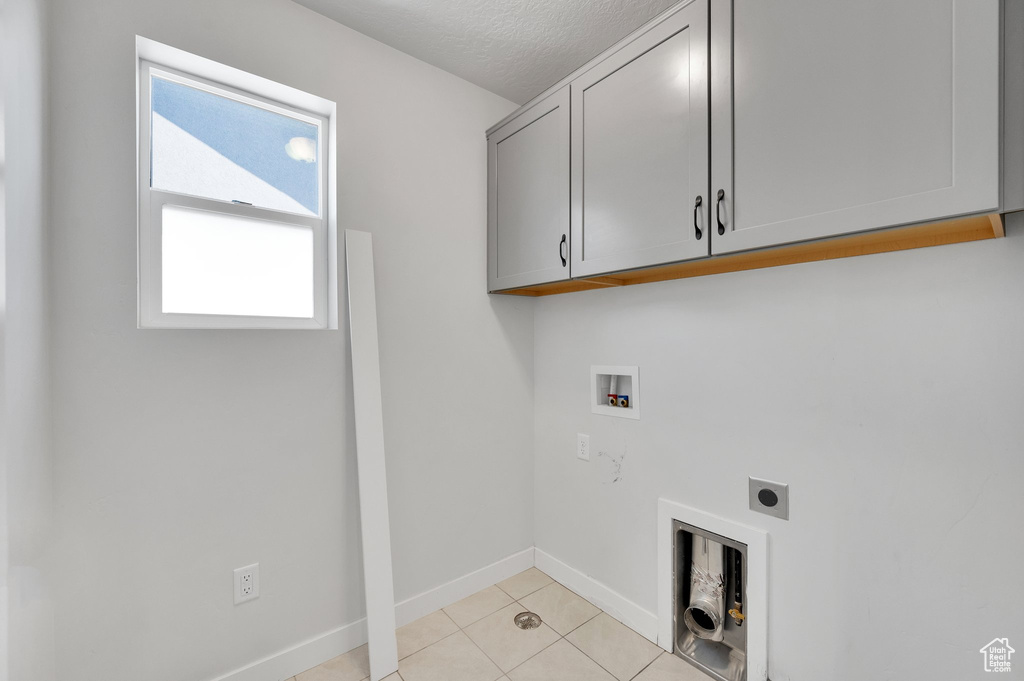 Laundry area with electric dryer hookup, cabinet space, hookup for a washing machine, a textured ceiling, and light tile patterned floors
